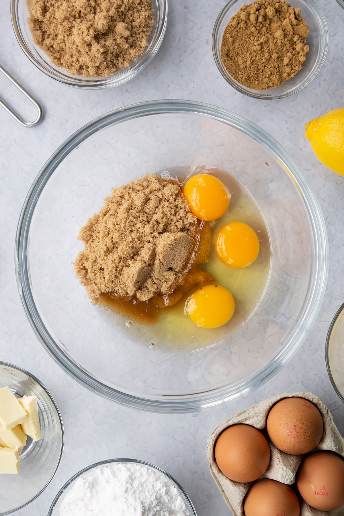 Eggs and light soft brown sugar in a glass mixing bowl. Ingredients to make Gingerbread Swiss roll surround the bowl.