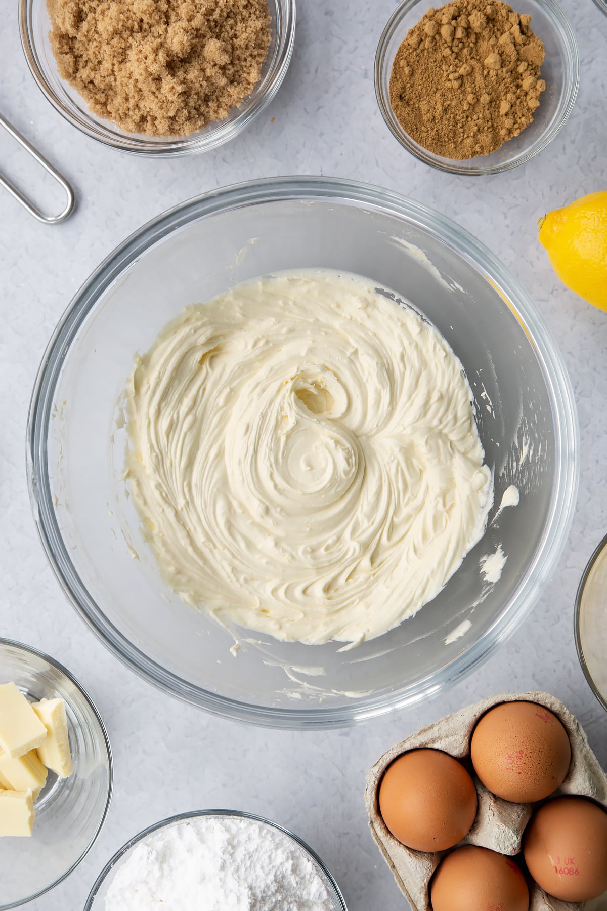 Lemon white chocolate buttercream in a glass mixing bowl. Ingredients to make Gingerbread Swiss roll surround the bowl.