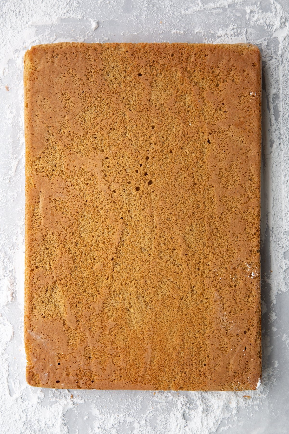 Baked gingerbread Swiss roll sponge, face down on a surface dusted with icing sugar. Backing paper removed.