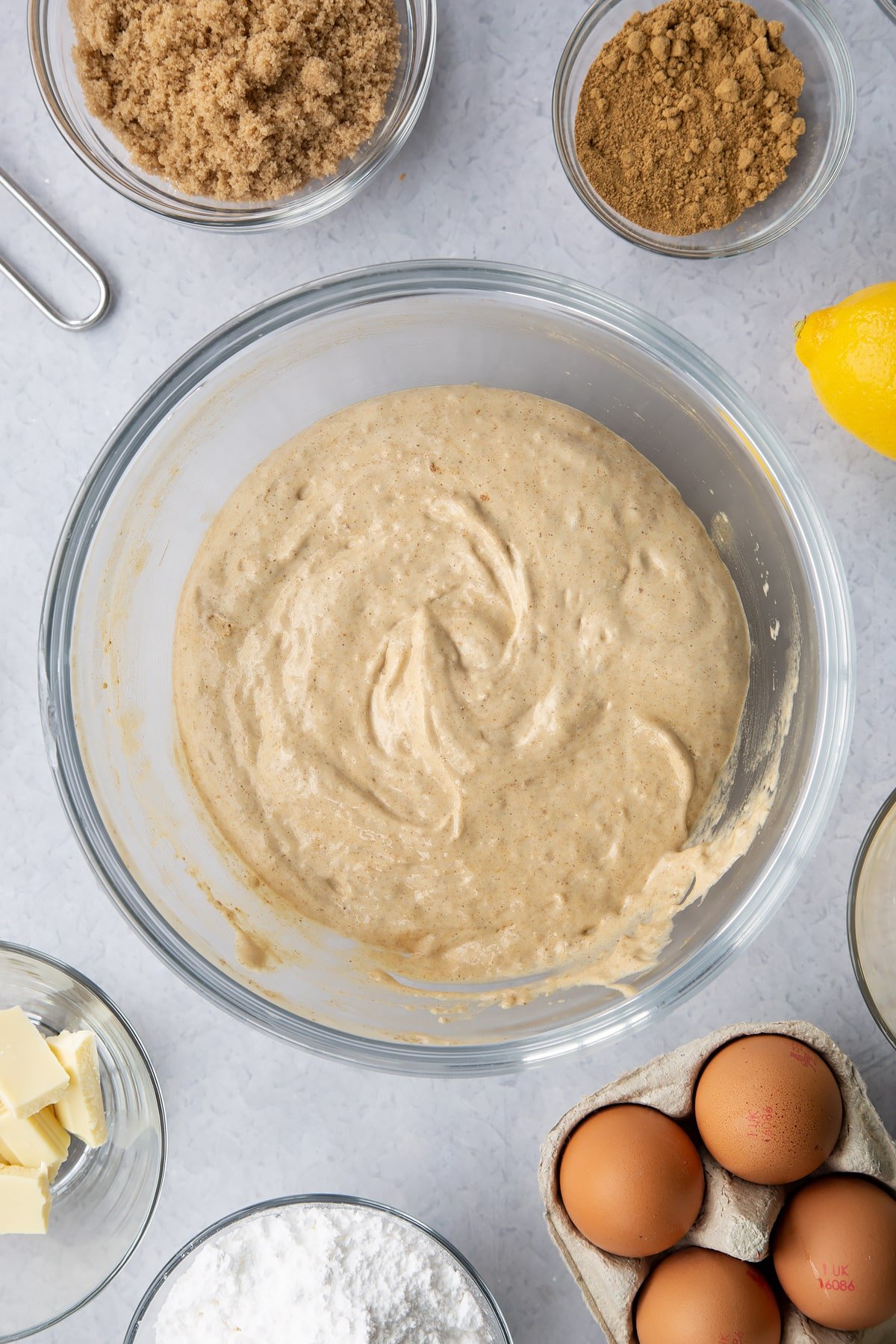 Gingerbread Swiss roll sponge batter in a glass mixing bowl. Ingredients to make Gingerbread Swiss roll surround the bowl.