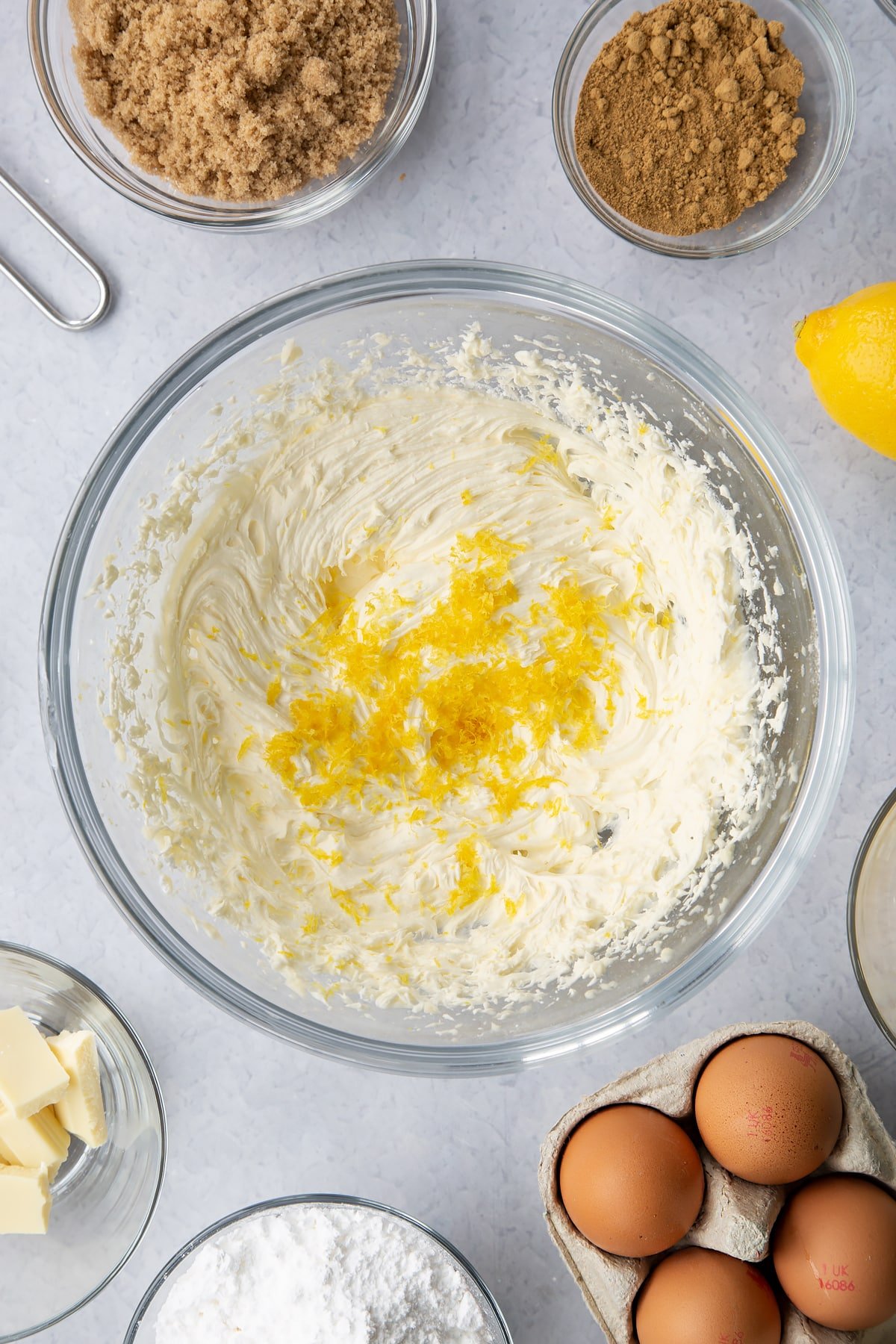 Buttercream in a glass mixing bowl with lemon zest on top. Ingredients to make Gingerbread Swiss roll surround the bowl.