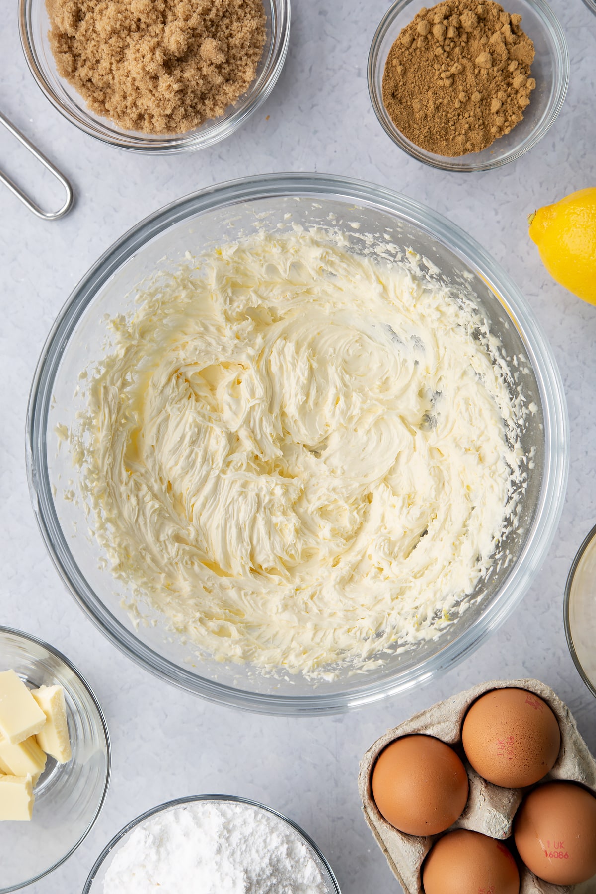 Lemon buttercream in a glass mixing bowl. Ingredients to make Gingerbread Swiss roll surround the bowl.