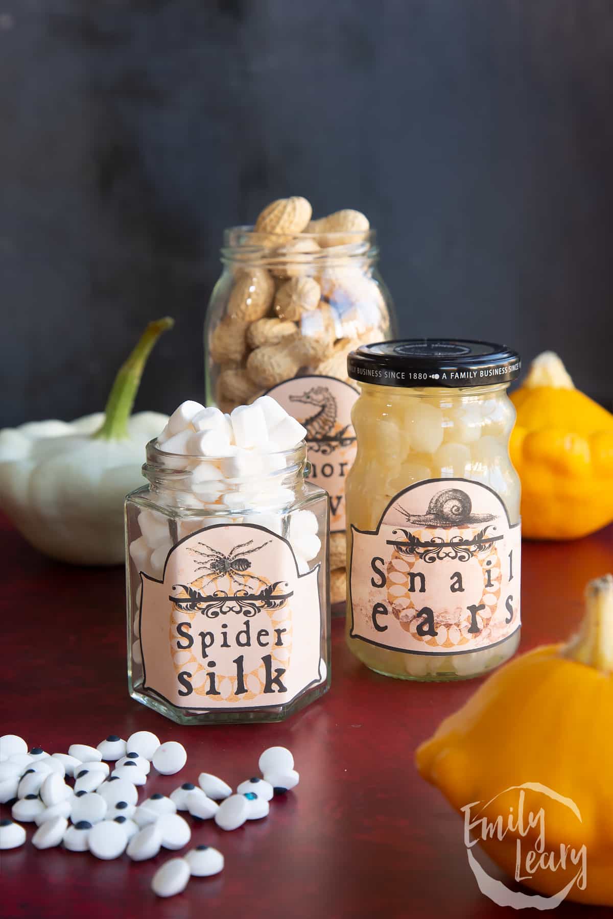 Three jars of different sizes, bearing Halloween apothecary labels. The jars contain mini marshmallows (Spider silk), Monkey Nuts (Seahorse hooves) and baby pickled onions (Snail ears).