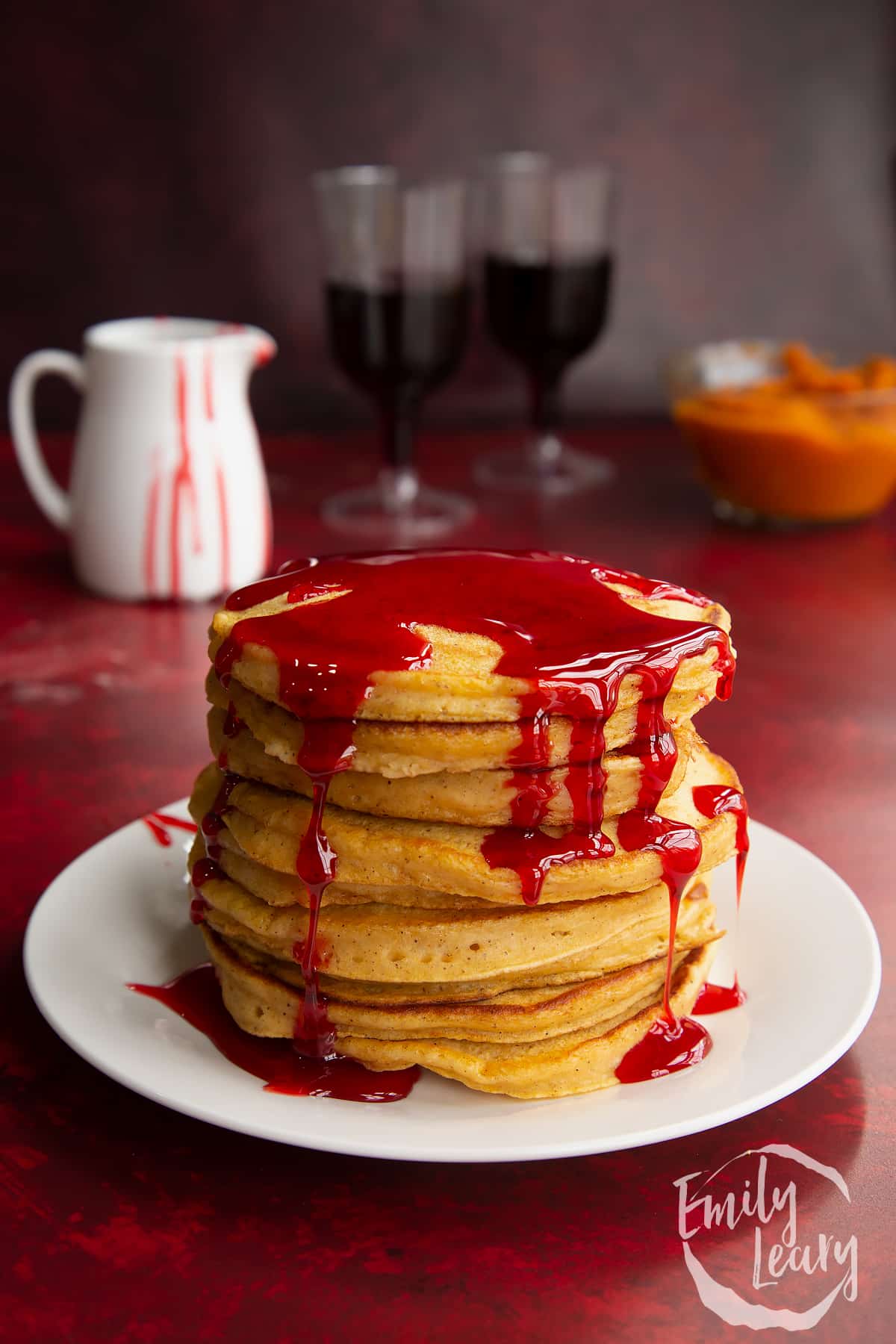 Halloween pancakes stacked on a white plate, drizzled with red syrup. 