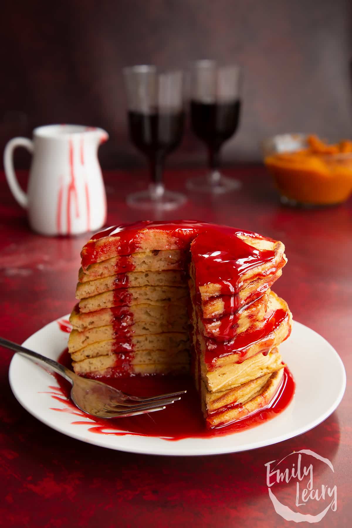 Halloween pancakes stacked on a white plate, drizzled with red syrup. A section has been cut away. A fork rests on the plate. 