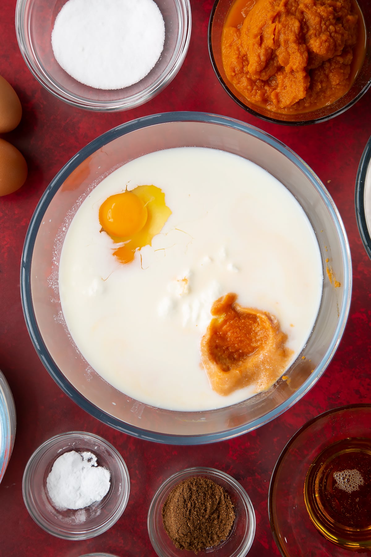 Yogurt, egg, milk and pumpkin puree in a glass mixing bowl. Ingredients to make Halloween pancakes surround the bowl.