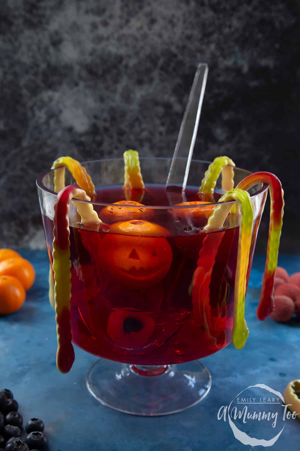 Halloween punch in a glass punch bowl. It is a red liquid, decorated with gummy snakes, jack'o'lantern clementines and lychee and blueberry eyeballs.