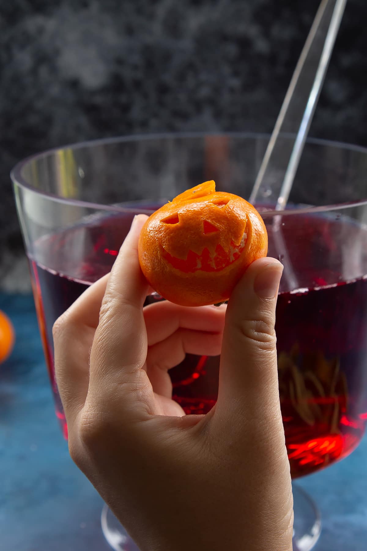 A hand holding a clementine trimmed to look like a jack'o'lantern.