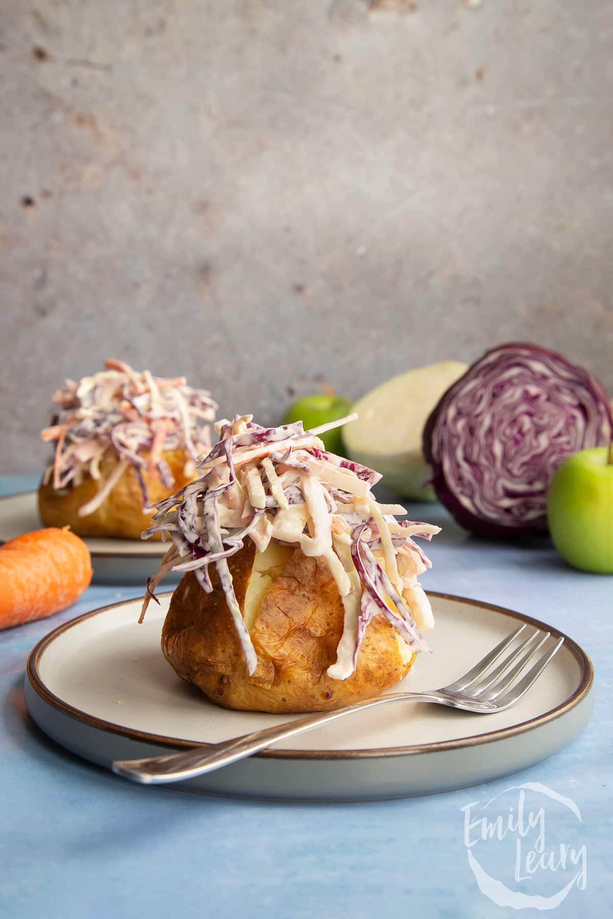 side view of coleslaw on top of a jacket potato on a white plate with a fork on the side.