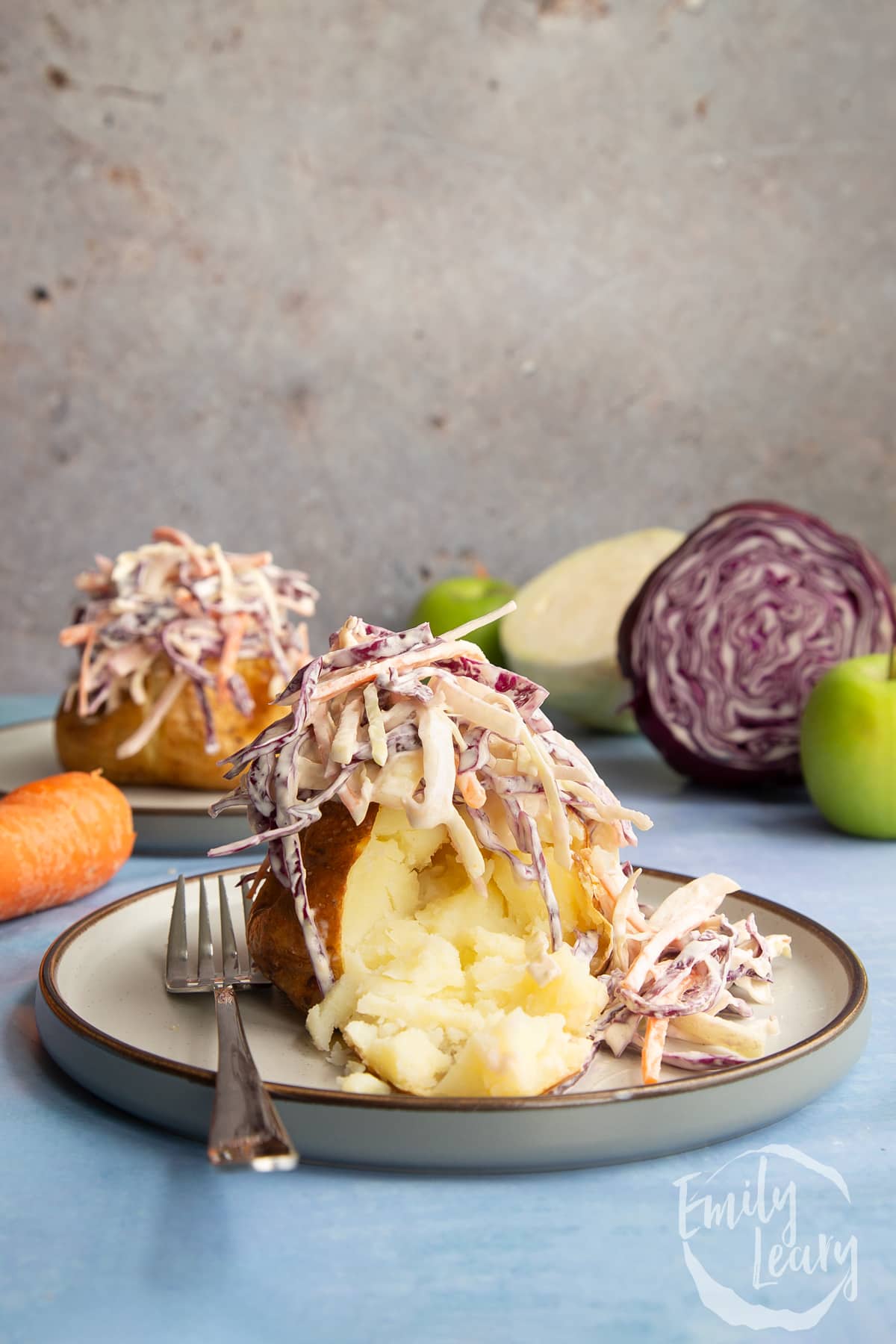 side view of coleslaw on top of a jacket potato on a white plate with a fork on the side.