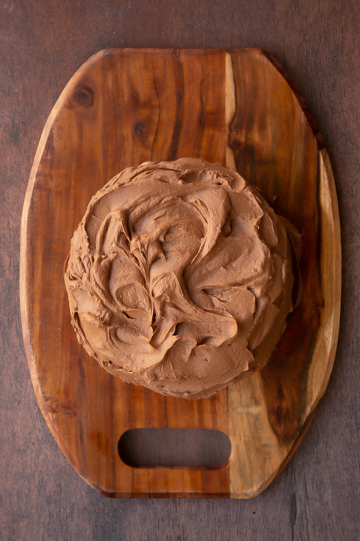 Two chocolate cake layers on a wooden board, sandwiched and topped with Matchmaker ganache.