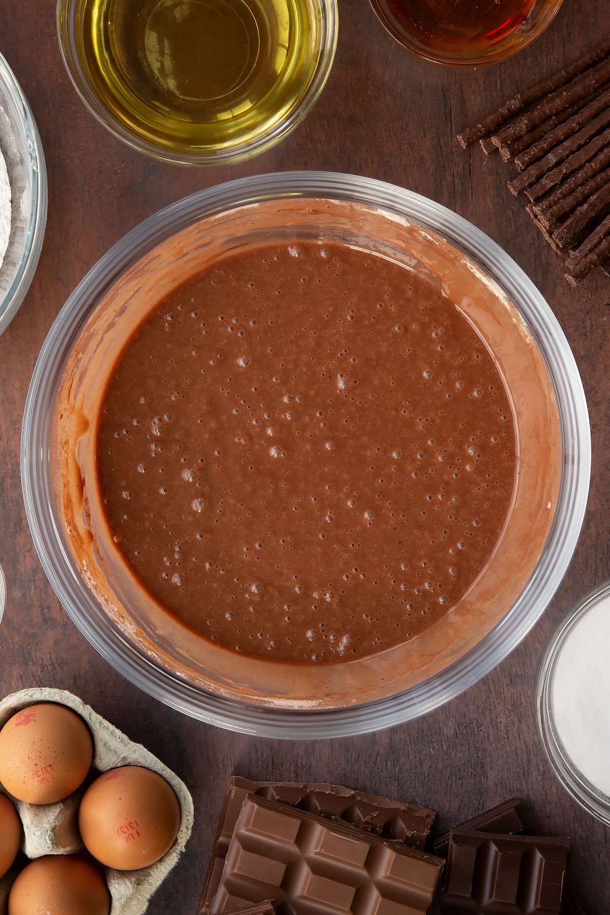 Chocolate cake batter in a glass mixing bowl. Ingredients to make Matchmaker cake surround the bowl. 