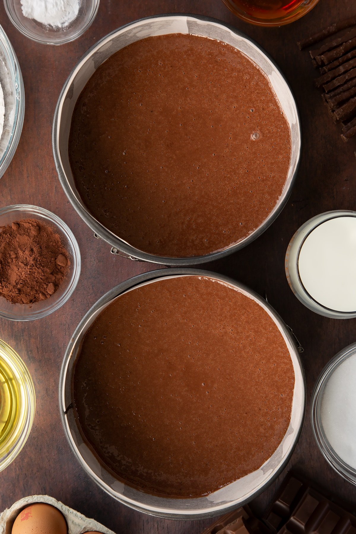 Chocolate cake batter in a two lined baking tins. Ingredients to make Matchmaker cake surround the tins.