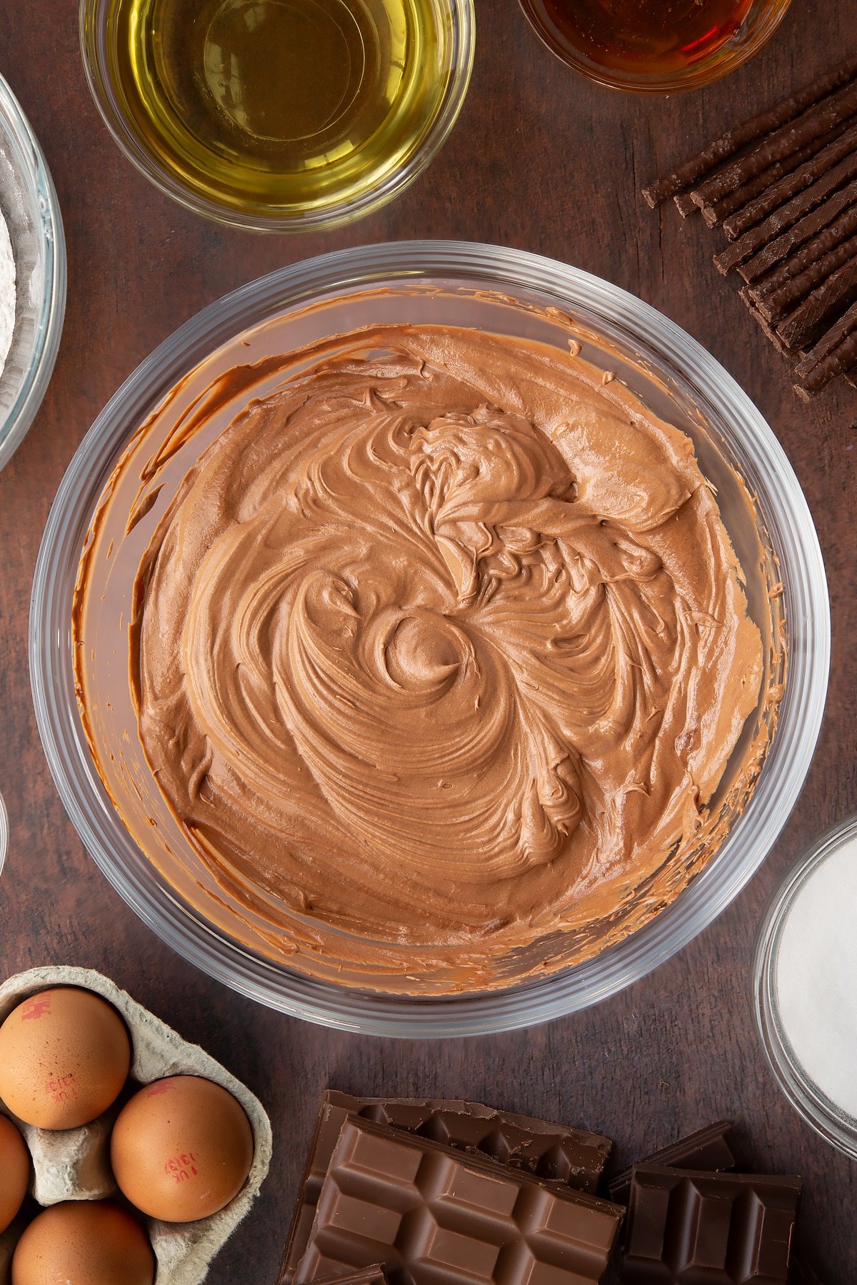 Whipped Matchmaker ganache in a glass mixing bowl. Ingredients to make Matchmaker cake surround the bowl.