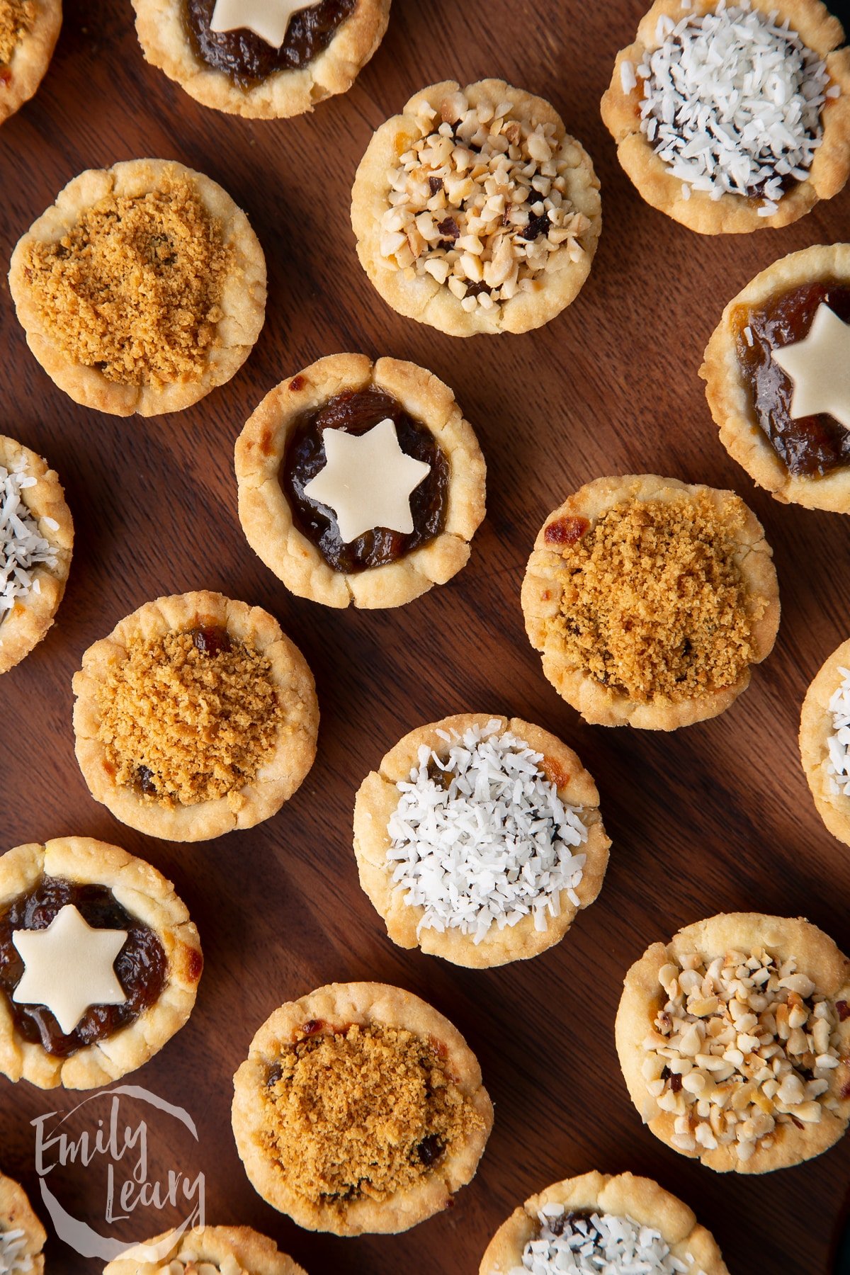 Close up on mini mince pies, shown from above on a dark wooden board. 