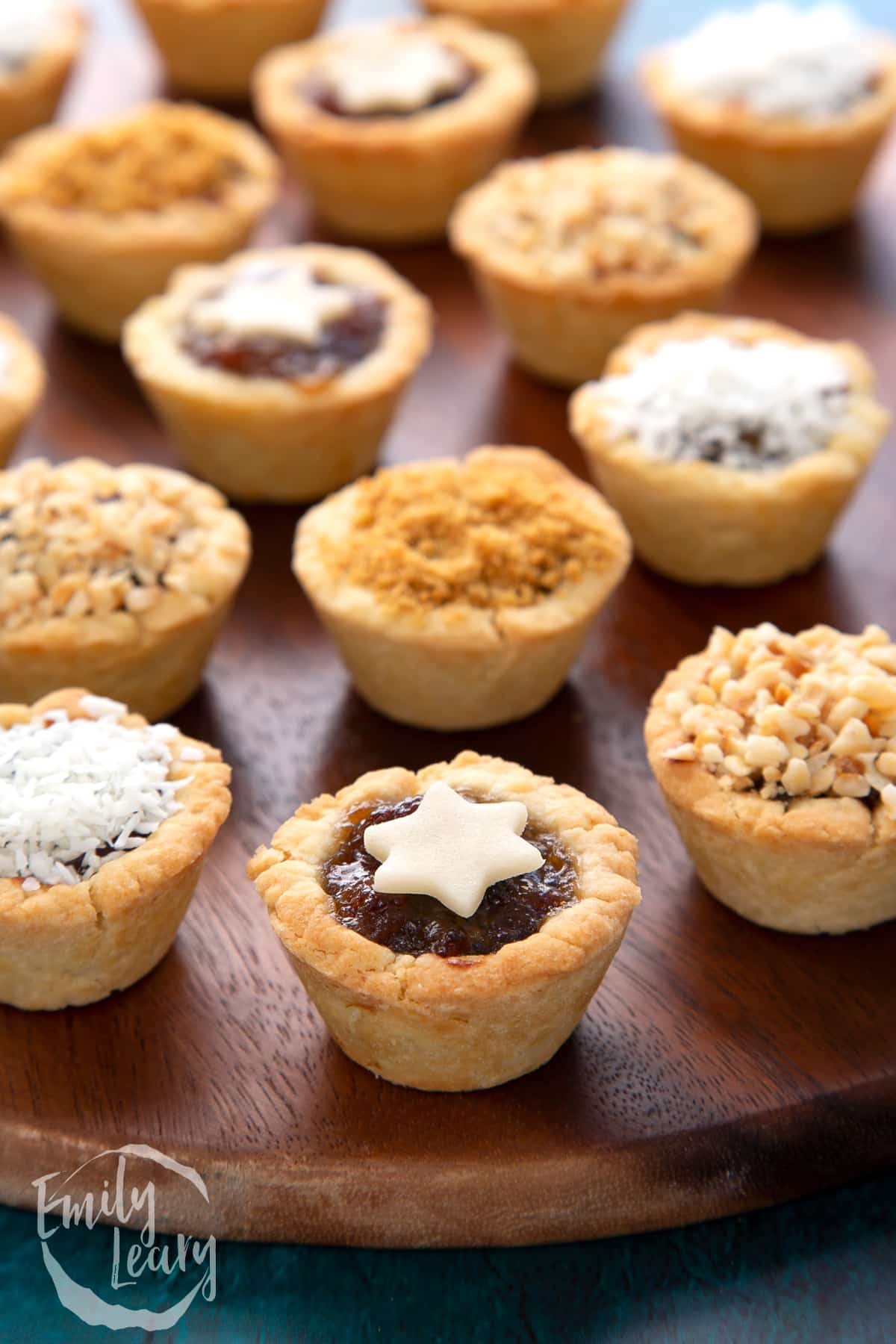 A marzipan star topped mini mince pie. More mini mince pies are also on the dark wooden board.