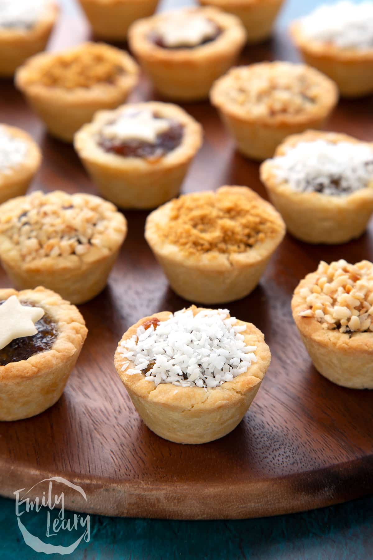 A desiccated coconut topped mini mince pie. More mini mince pies are also on the dark wooden board.