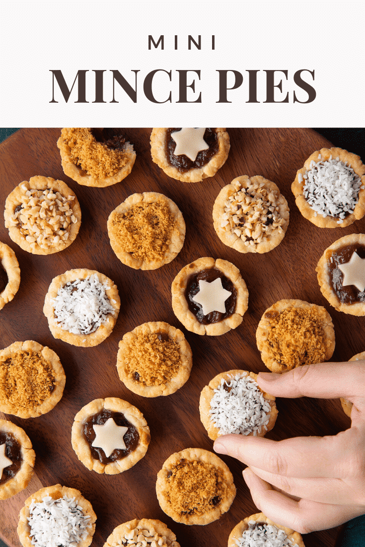 Mini mince pies on a dark wooden board, shown from above. A hand takes one. Caption reads: Mini mince pies.