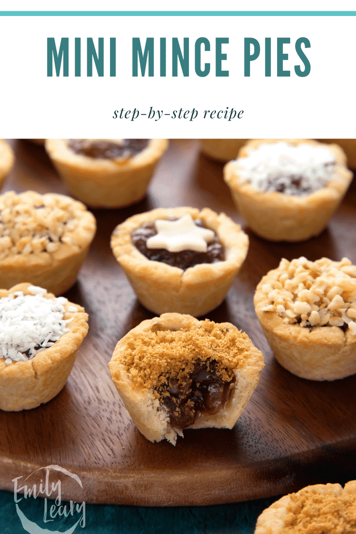 Mini mince pie on a dark wooden board, topped with gingernut crumbs with a bite out of it. Caption reads: Mini mince pies.