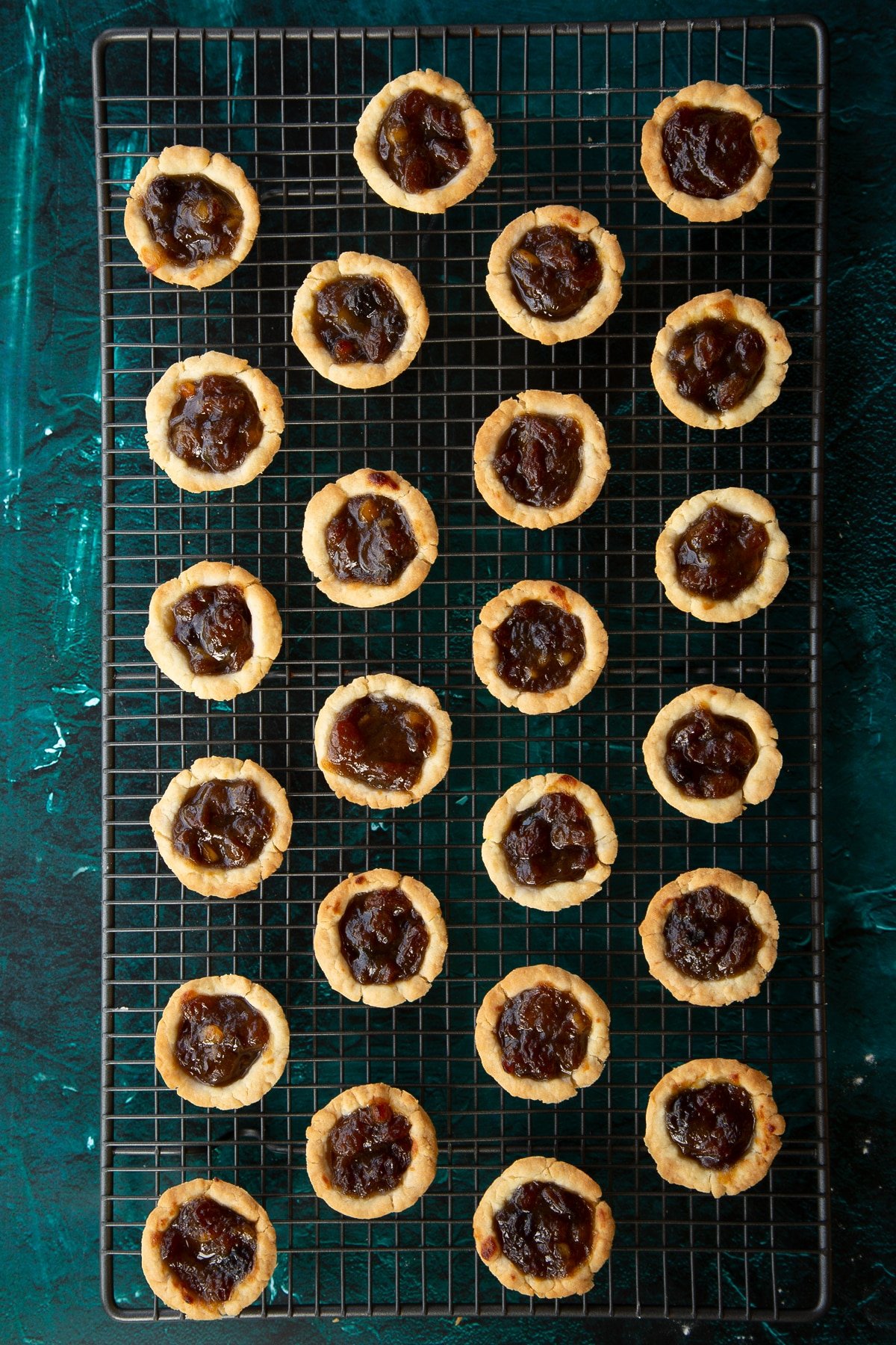 Freshly baked mini mince pies on a cooling rack.