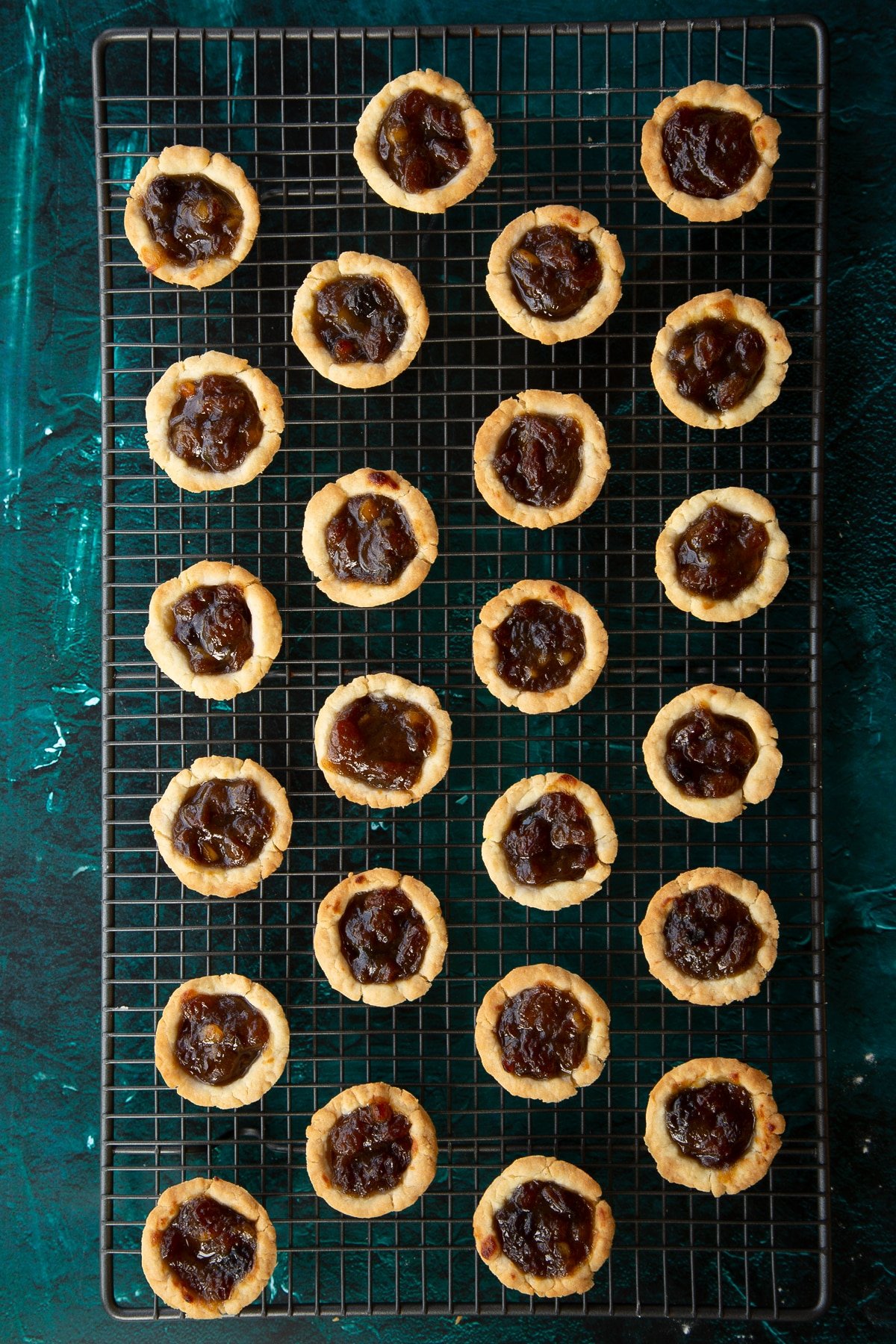 Freshly baked mini mince pies on a cooling rack.