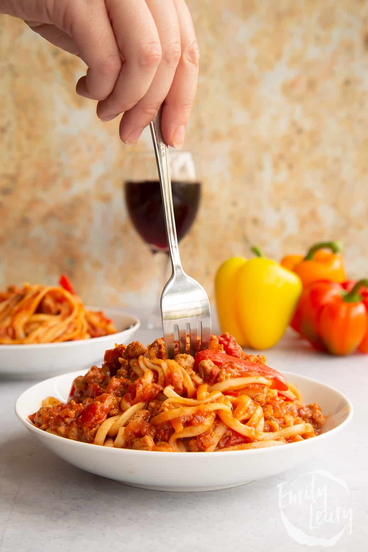 One pot vegan bolognese in a shallow white bowl. A hand holds a fork delving into the bowl.