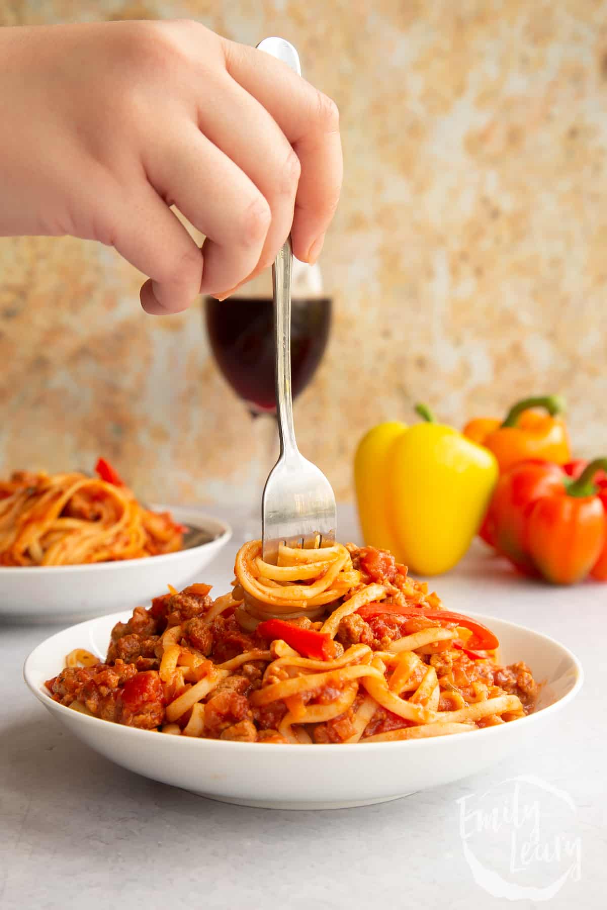 One pot vegan bolognese in a shallow white bowl. A hand holds a fork, twisting spaghetti in the bowl.