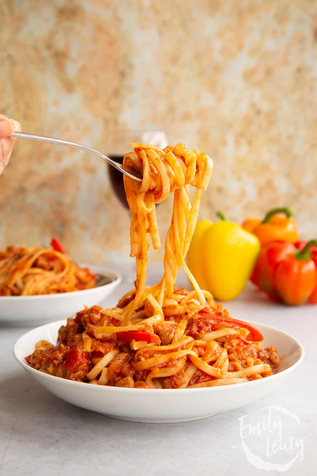 One pot vegan bolognese in a shallow white bowl. A hand lifts spaghetti from the bowl.