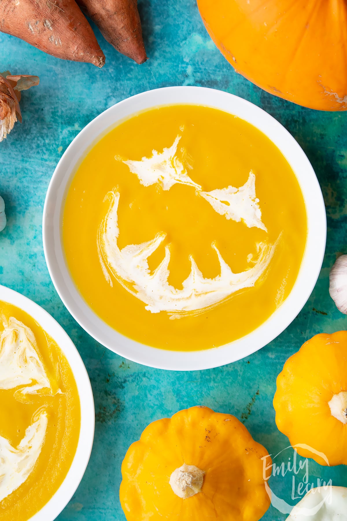 Pumpkin and sweet potato soup in a white bowl, from above. The soup has cream swirled on top to resemble a jack'o'lantern.