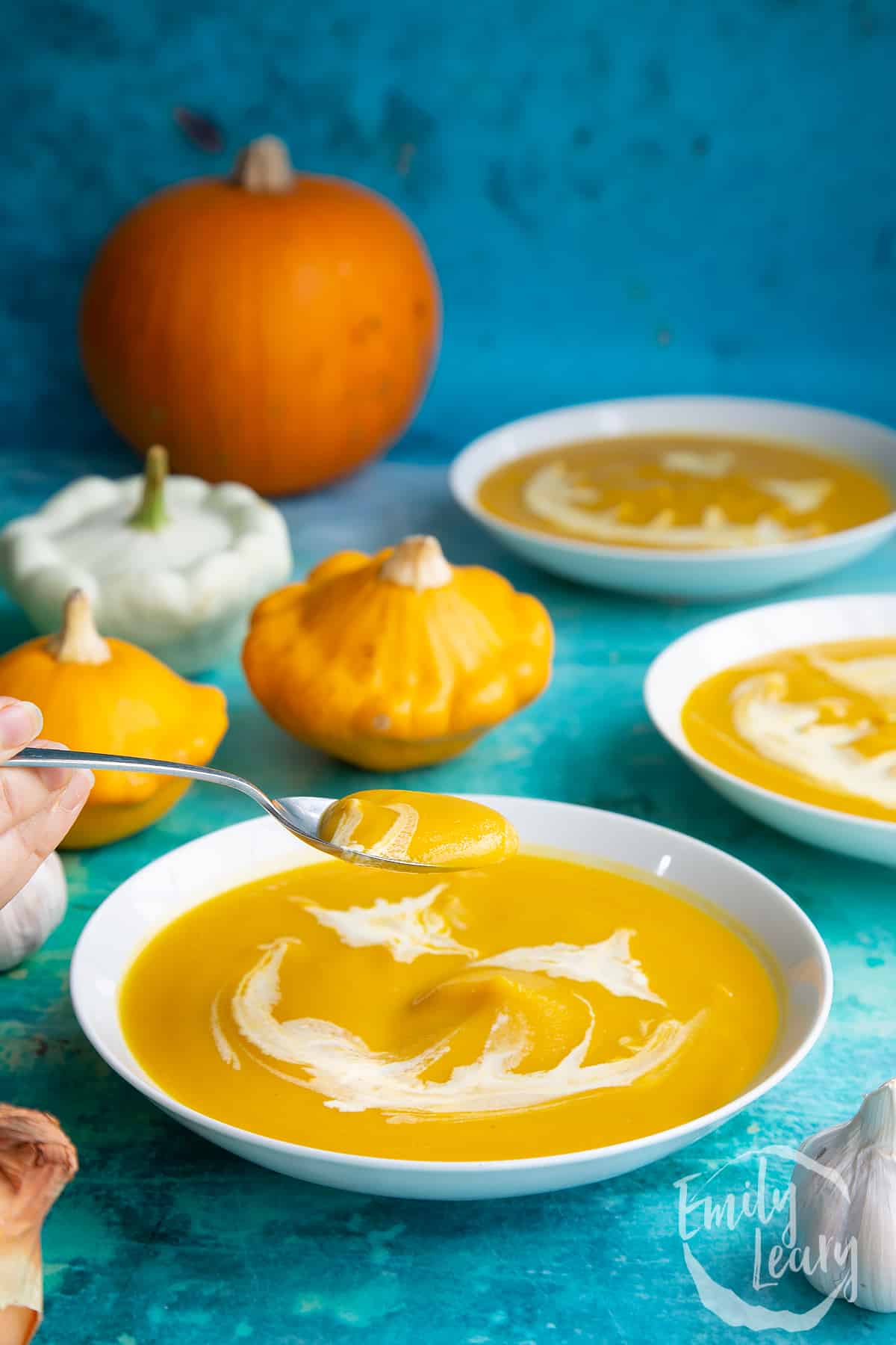 Pumpkin and sweet potato soup in a white bowl. The soup has cream swirled on top to resemble a jack'o'lantern. A spoon lifts some of the soup.