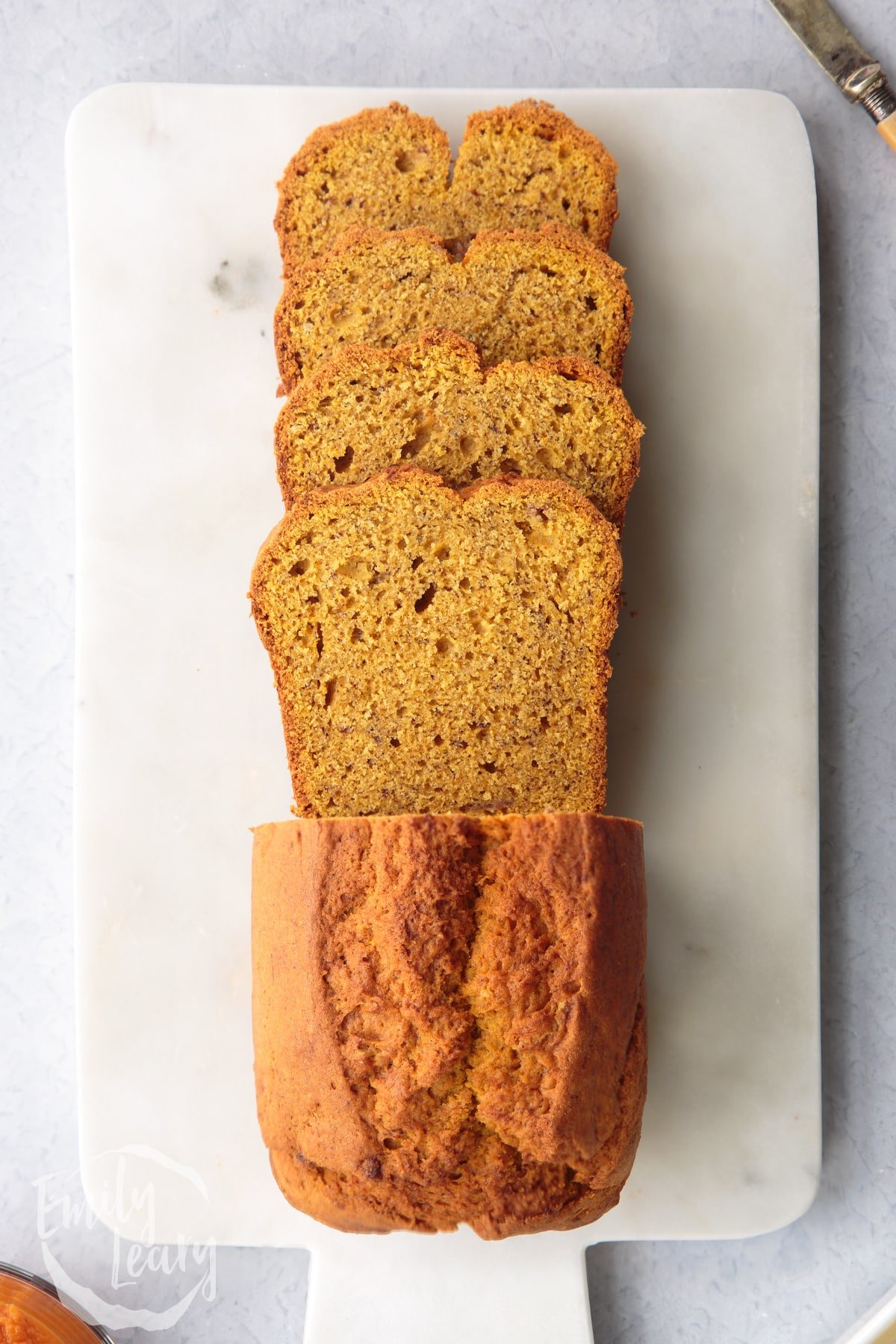 Pumpkin banana bread loaf on a white marble board. Some has been sliced.