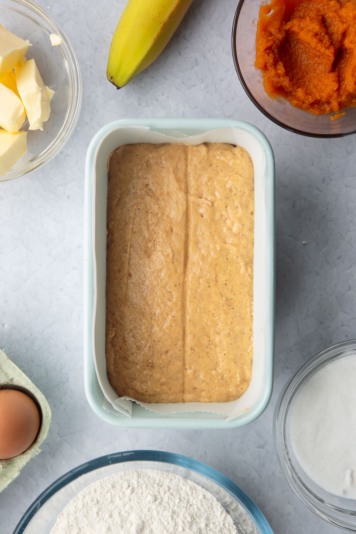 Pumpkin banana bread batter in a lined loaf tin with a line down the middle.