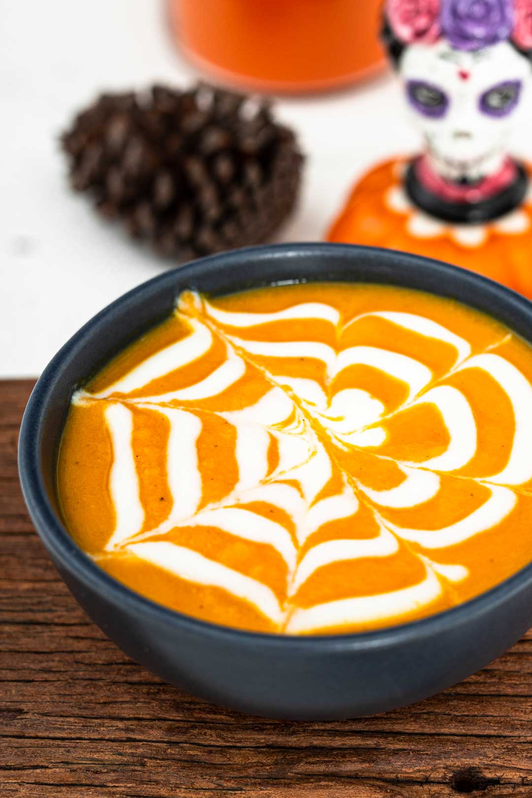 Carrot soup served into a dark bowl with a Halloween spiderweb drawn on the top in cream.