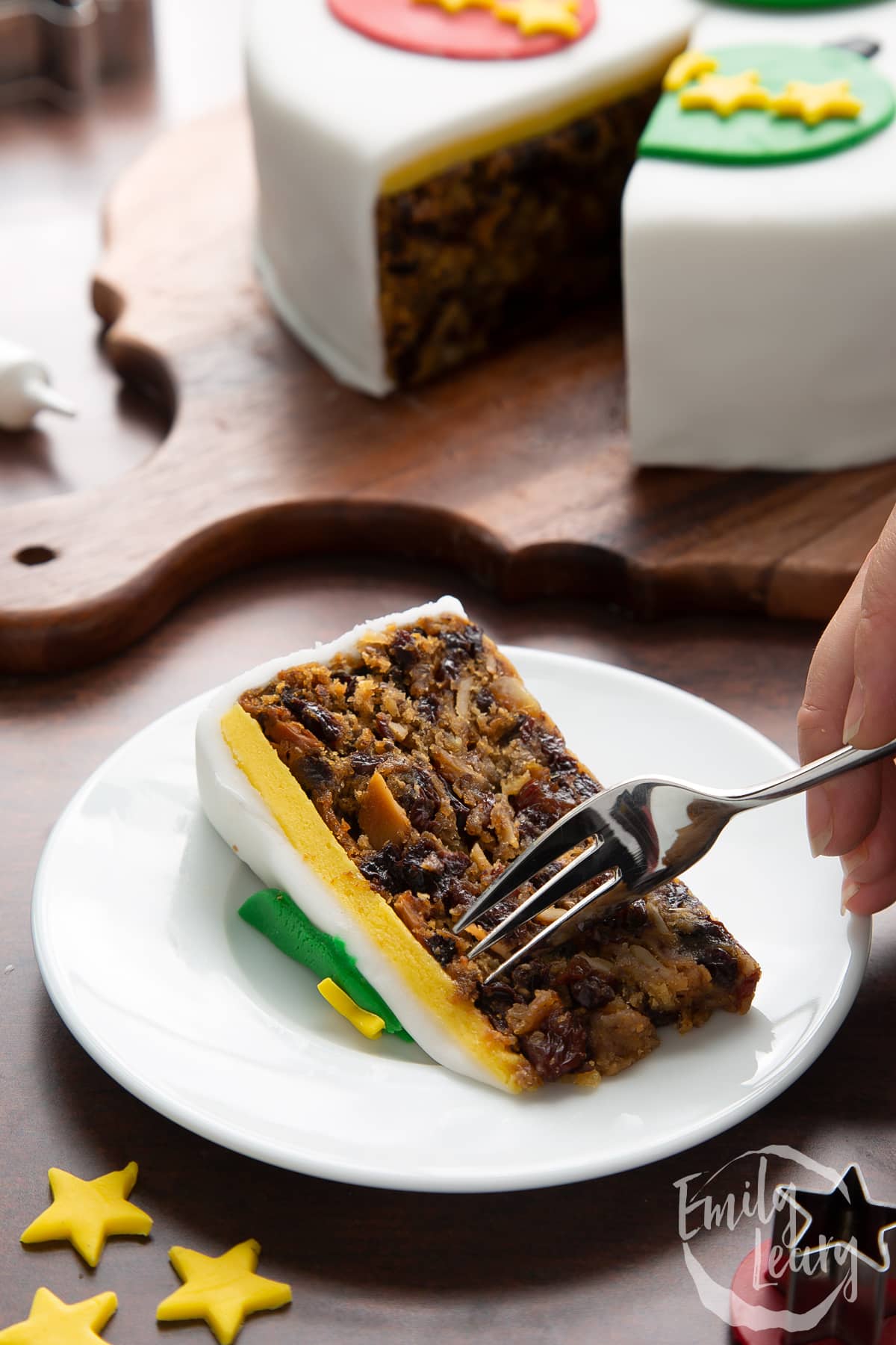 Slice of vegan Christmas cake on a white plate. A hand holds a fork.