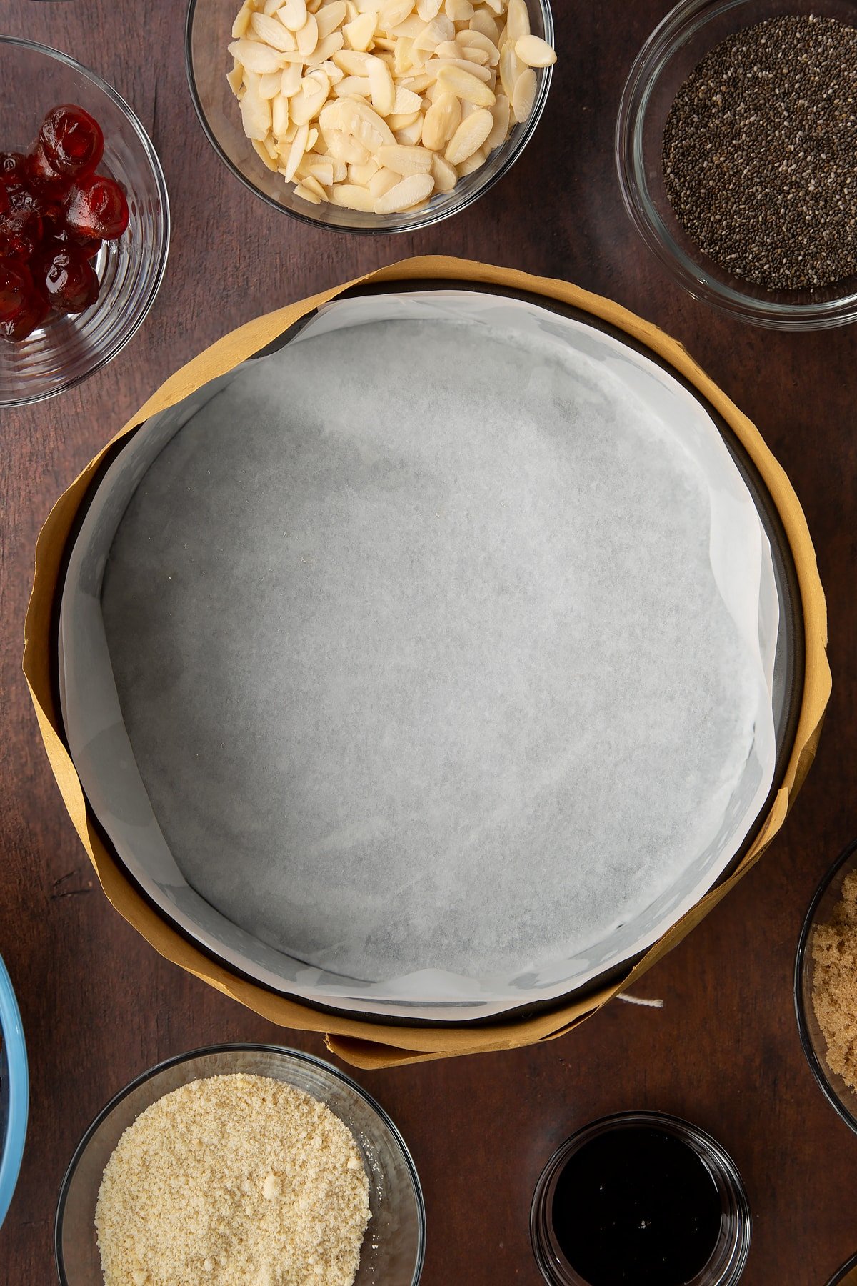 Cake tin lined with baking paper and wrapped in brown paper, tied with string. Ingredients to make vegan Christmas cake surround the tin.