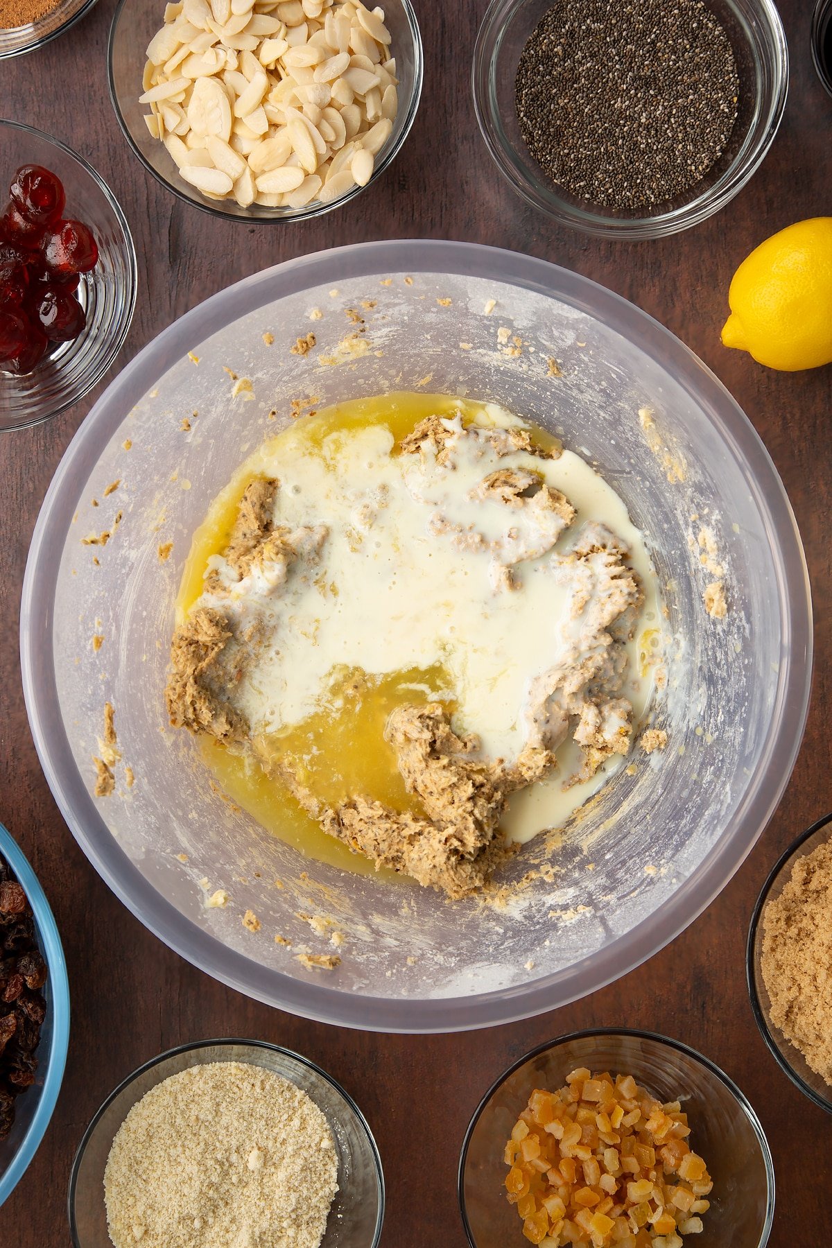 Butter, sugar, treacle, flour, almonds and spices in a bowl with plant milk, lemon juice and orange juice on top. Ingredients to make vegan Christmas cake surround the bowl.