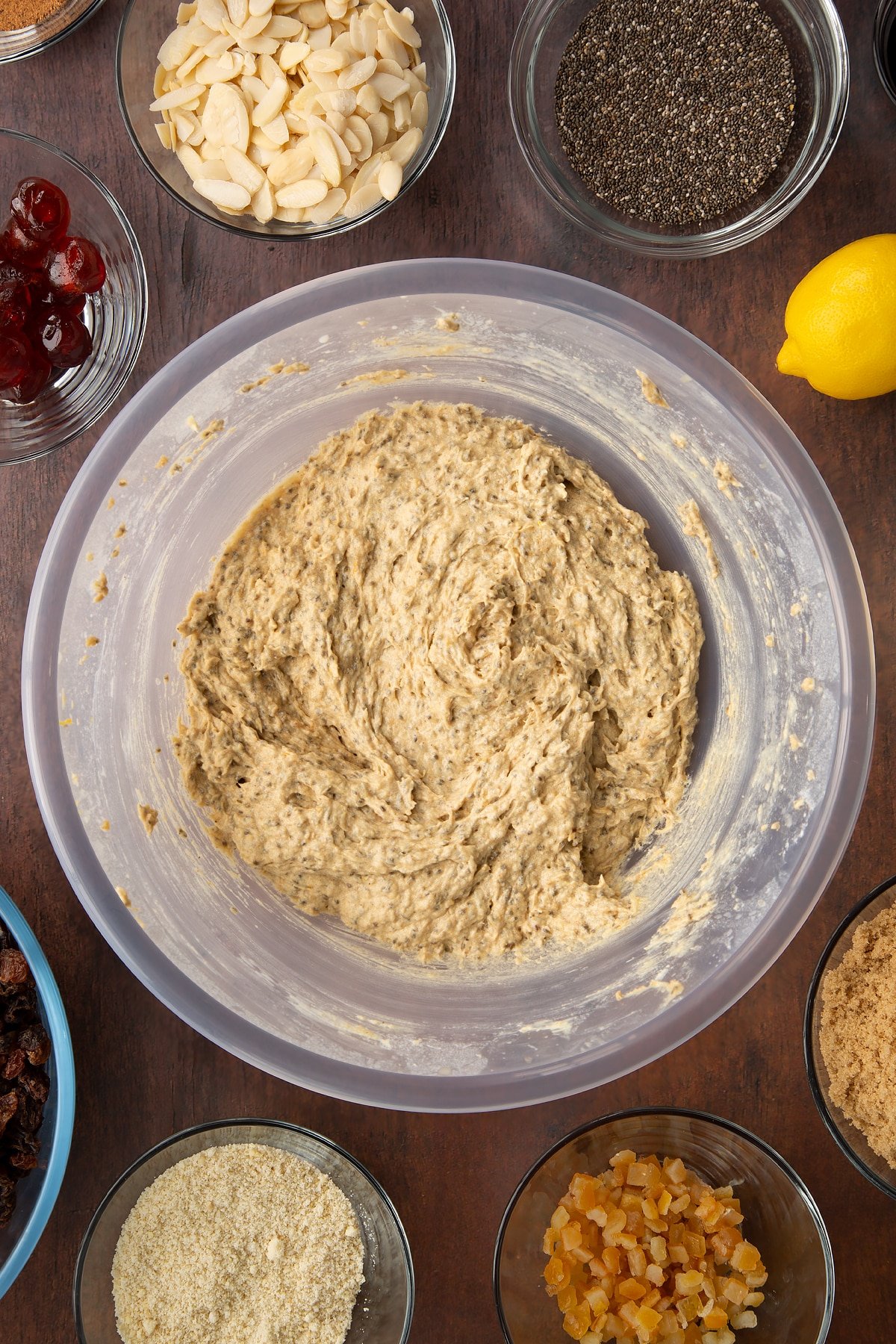 Butter, sugar, treacle, flour, almonds, spices, citrus juice and plant milk in a bowl. Ingredients to make vegan Christmas cake surround the bowl.