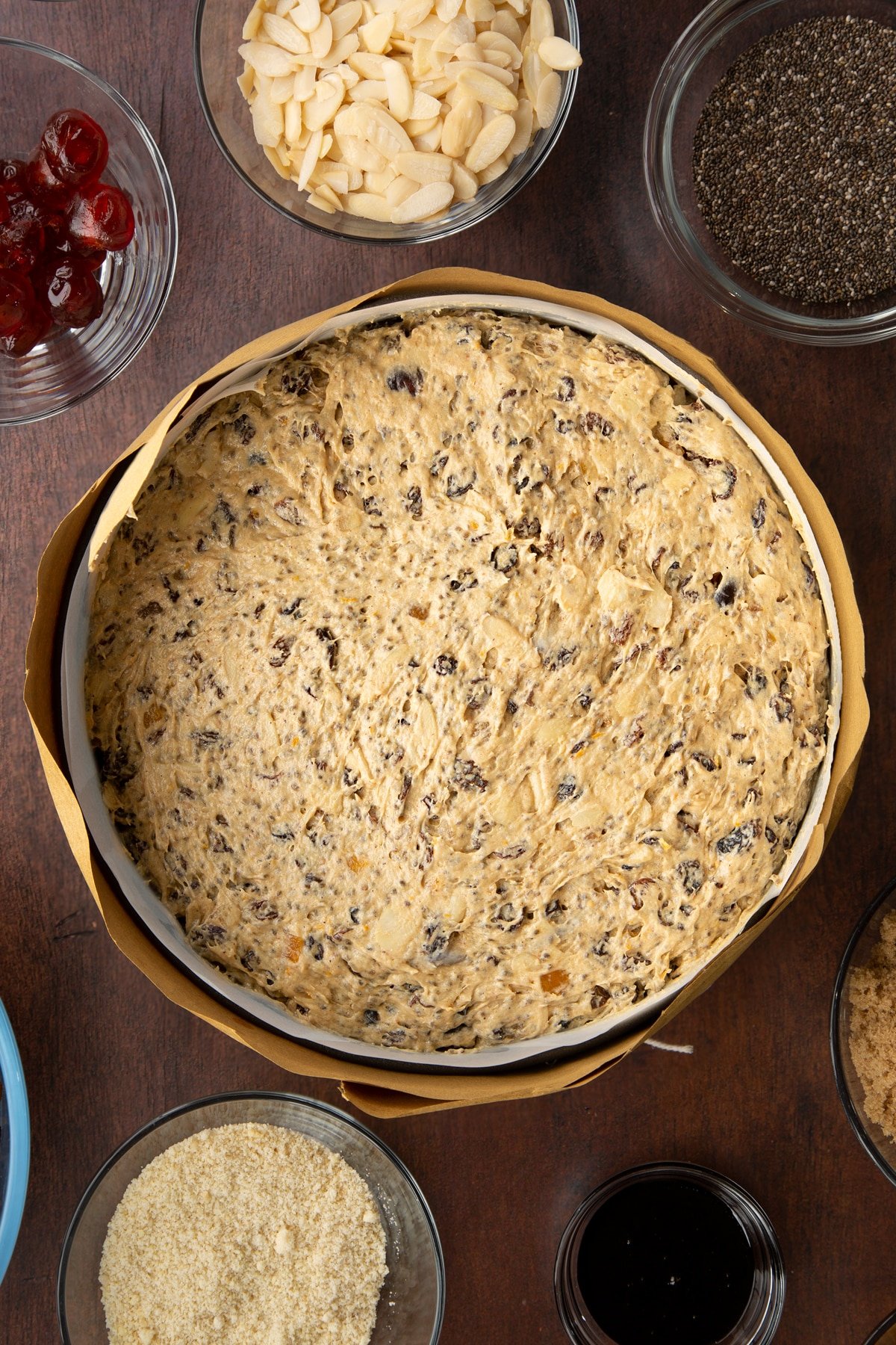 Vegan Christmas cake batter in a cake tin lined with baking paper and wrapped in brown paper, tied with string.