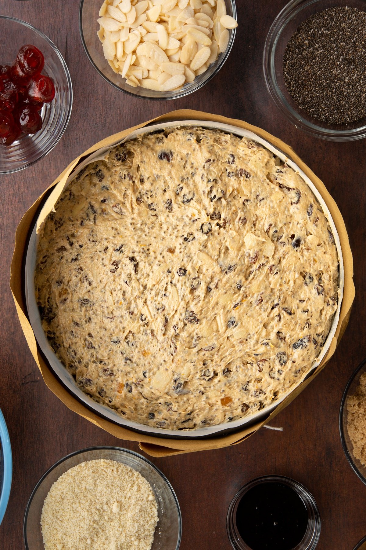 Vegan Christmas cake batter in a cake tin lined with baking paper and wrapped in brown paper, tied with string. 