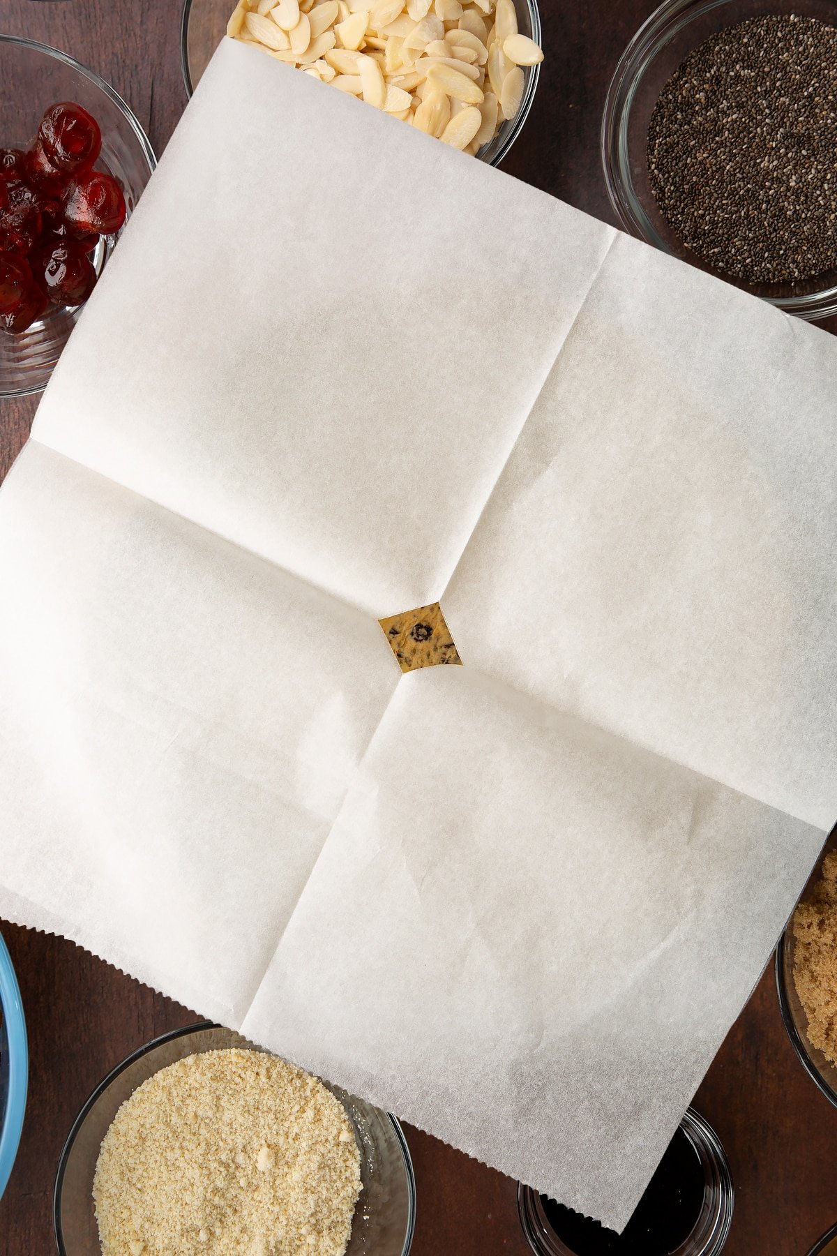 Vegan Christmas cake batter in a cake tin lined with baking paper and wrapped in brown paper, tied with string, topped with a square of baking paper.