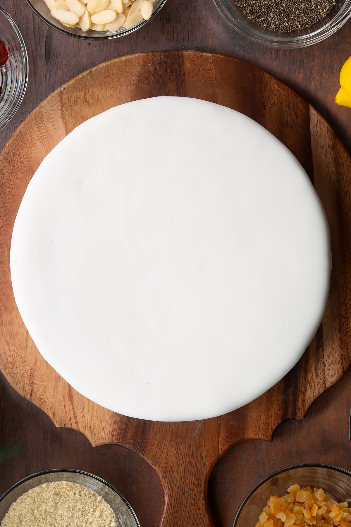 Vegan Christmas cake, topped with a disc of marzipan and covered with white sugar paste on a wooden board.