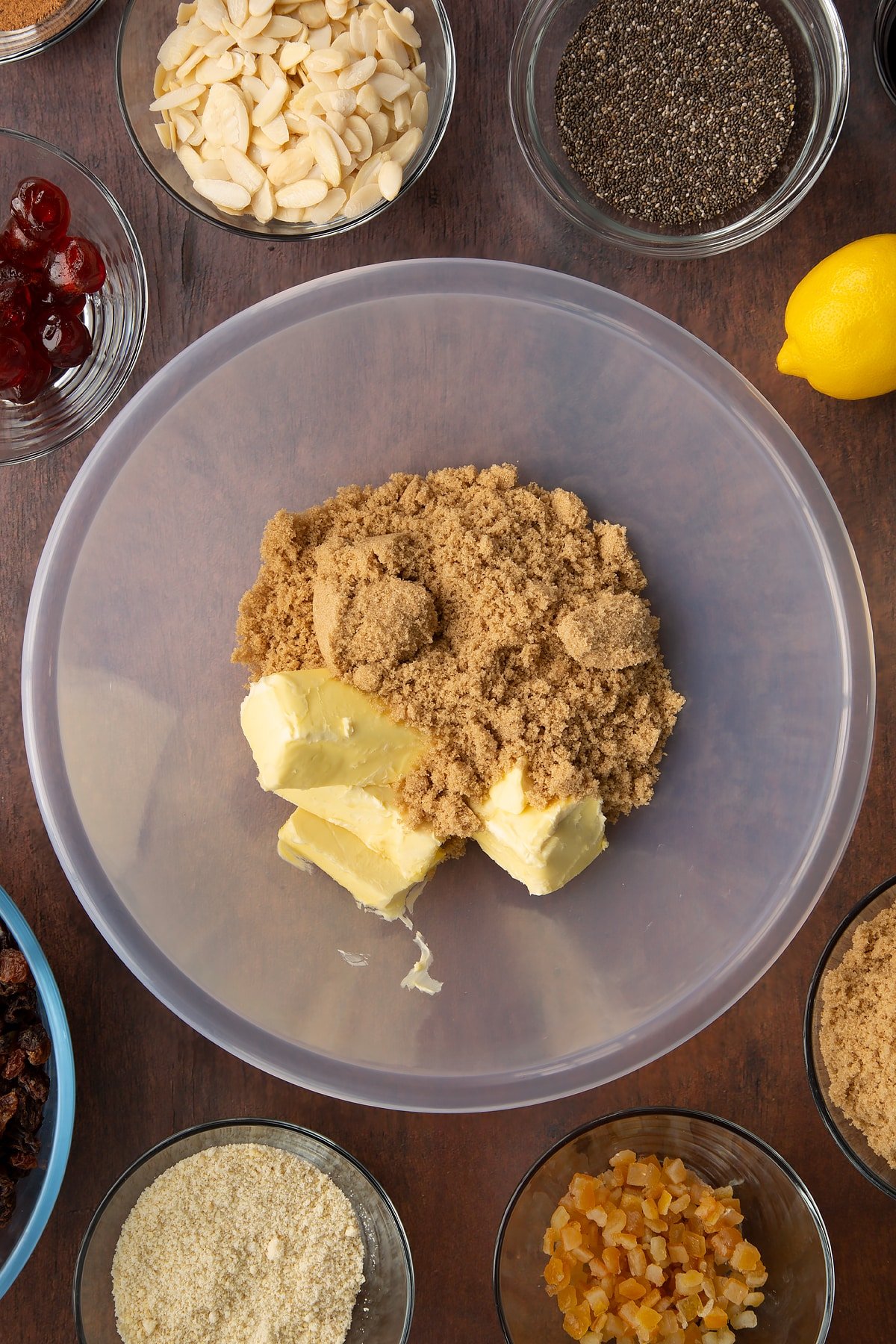 Vegan butter and brown sugar in a large plastic bowl. Ingredients to make vegan Christmas cake surround the bowl.