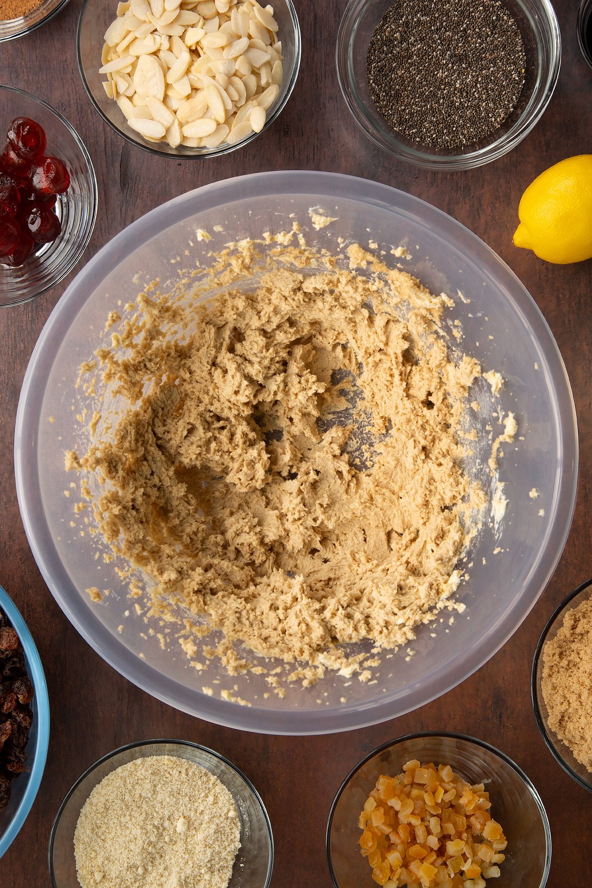 Vegan butter and brown sugar whisked together in a large plastic bowl. Ingredients to make vegan Christmas cake surround the bowl.