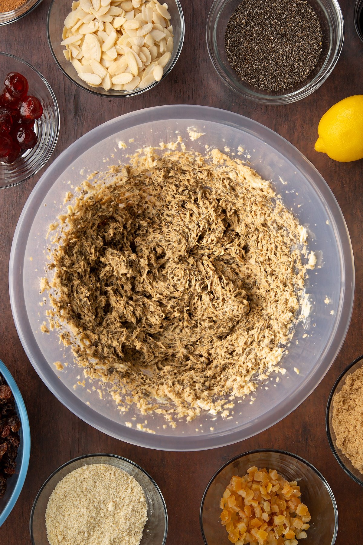 Vegan butter, brown sugar, chia "egg" and black treacle, whisked together in a large plastic bowl. Ingredients to make vegan Christmas cake surround the bowl.