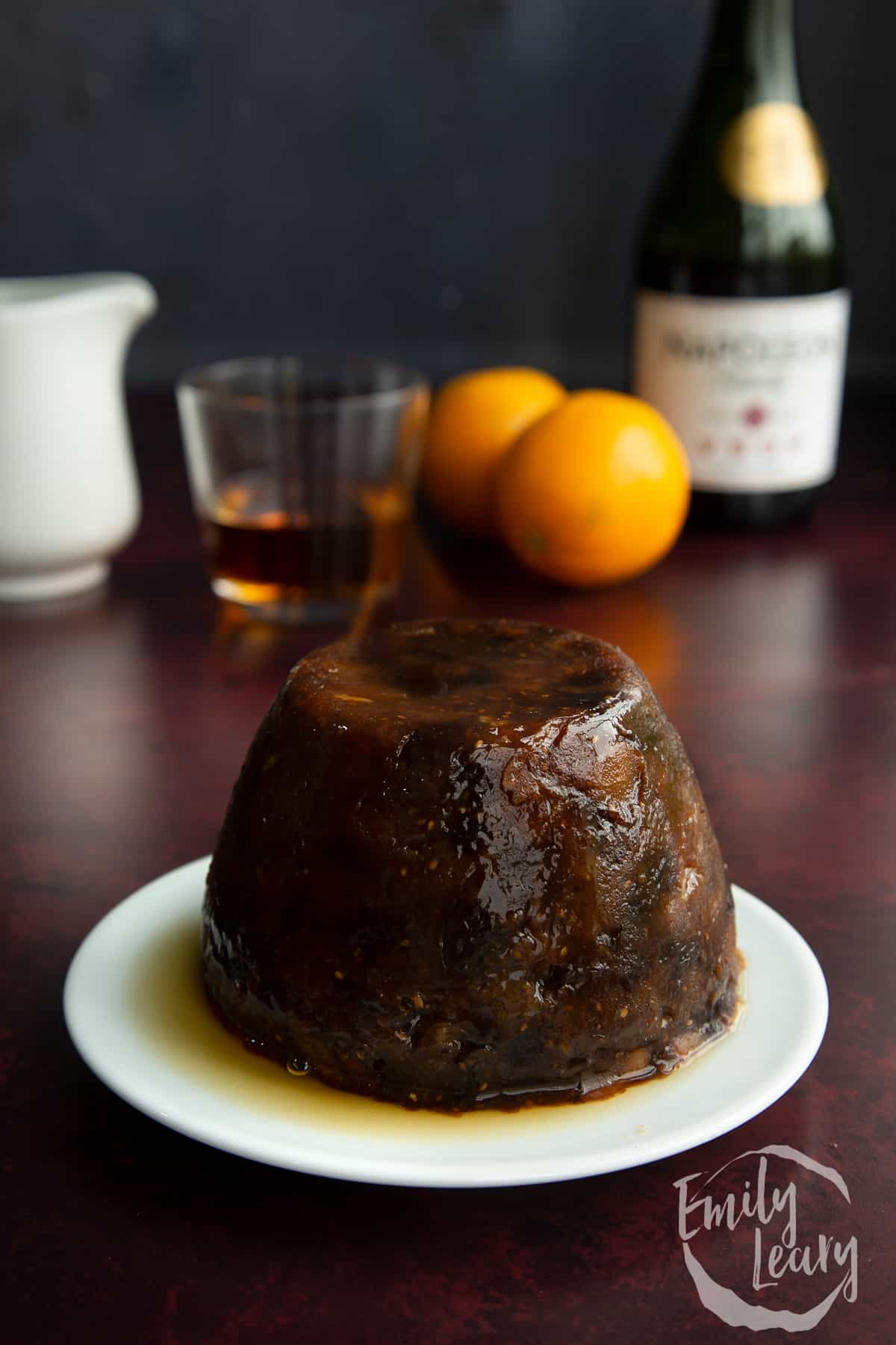 Steamed vegan Christmas pudding on a small white plate. It has lit whisky on it.