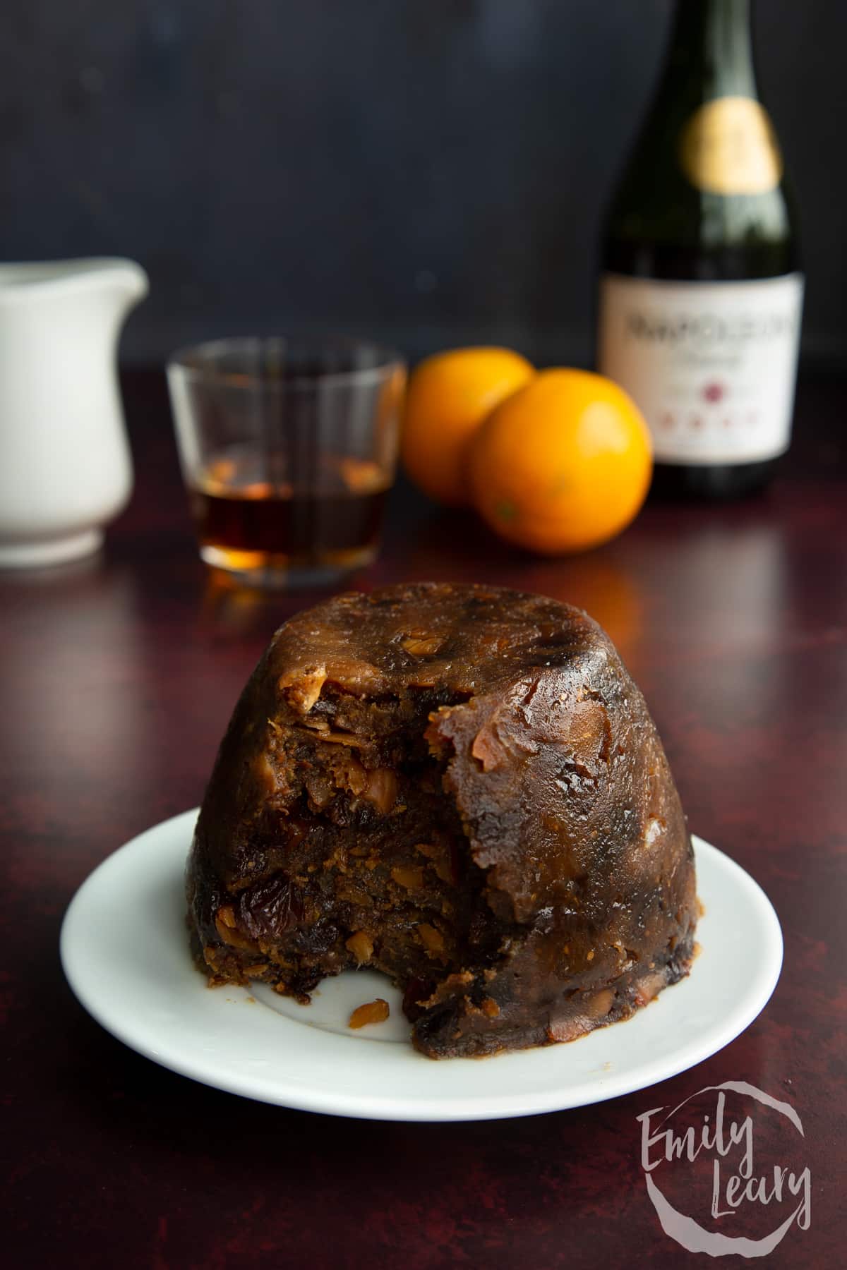 Steamed vegan Christmas pudding on a small white plate. Part has been spooned away.