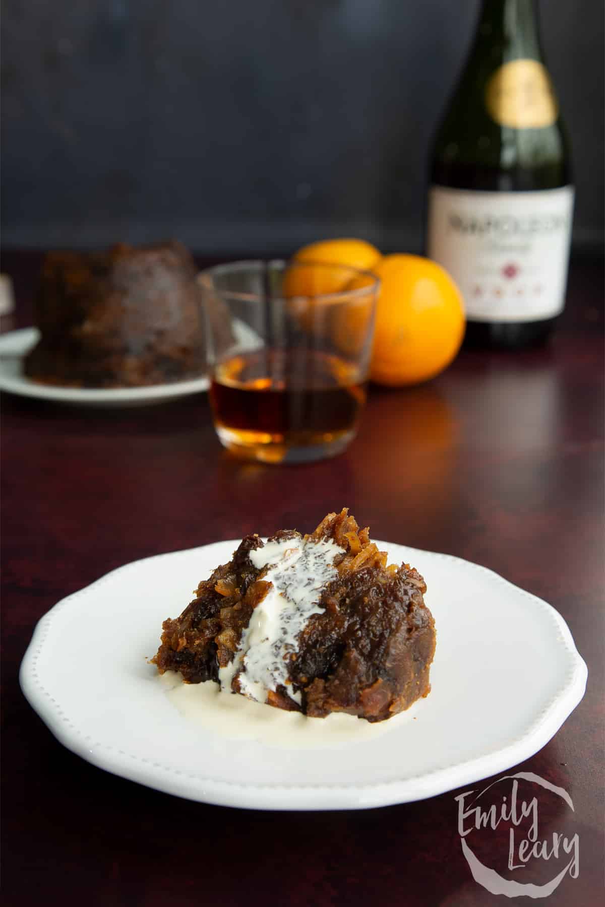 A piece of vegan Christmas pudding on a small white plate with vegan cream.