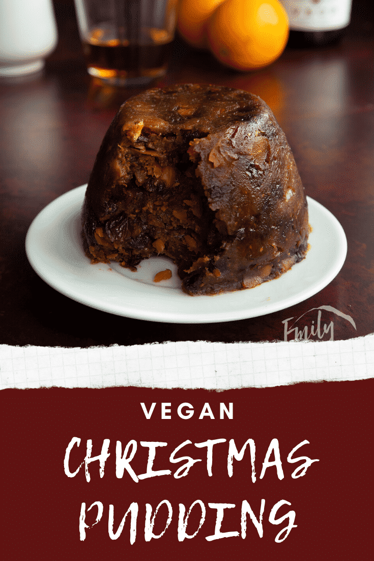 Steamed vegan Christmas pudding on a white plate. Some has been served. Caption reads: vegan Christmas pudding