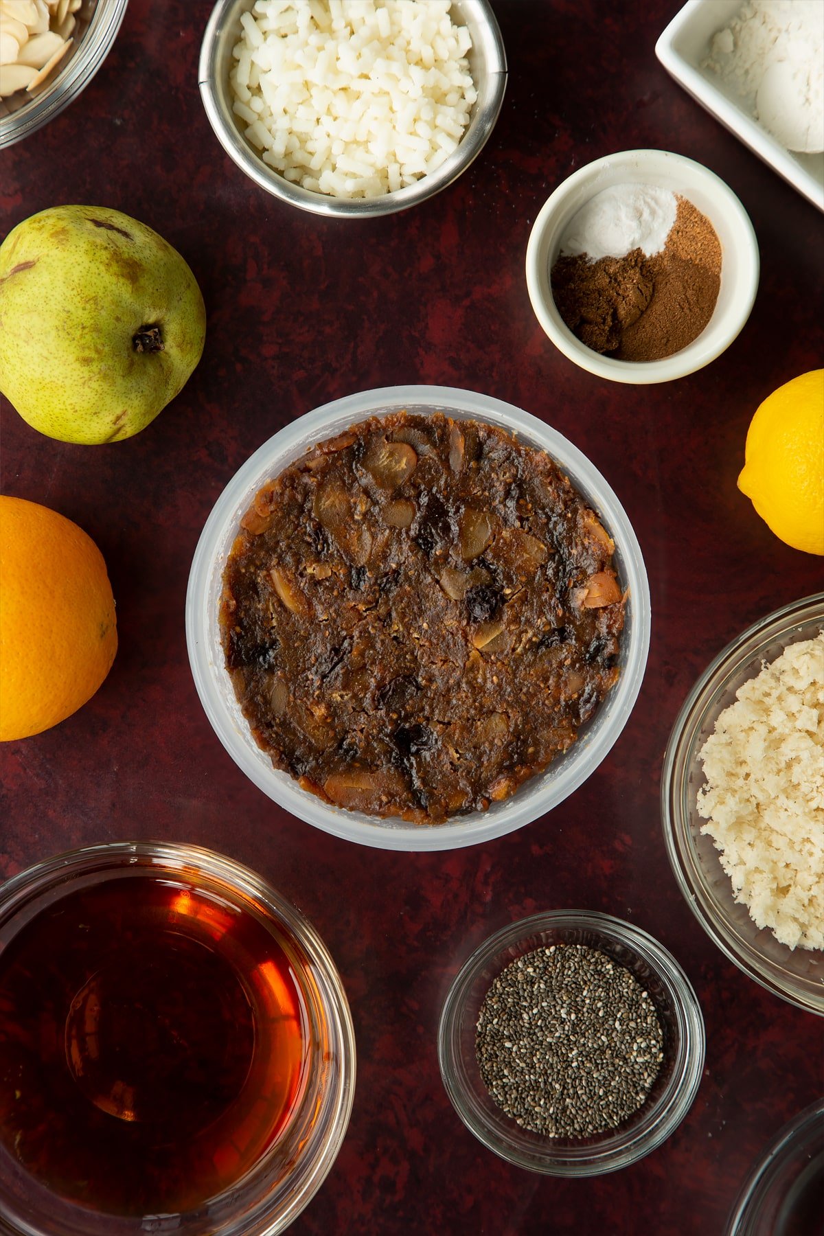 Steamed vegan Christmas pudding in a pudding basin. Ingredients to make vegan Christmas pudding surround the basin.