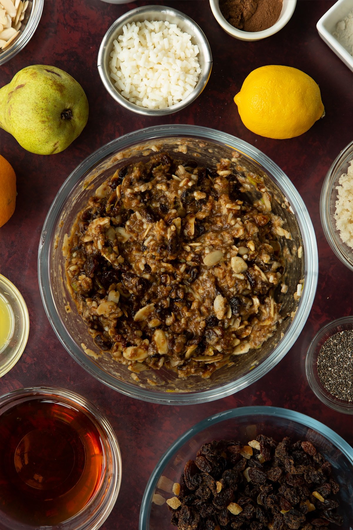 Vegan Christmas pudding batter in a glass bowl. Ingredients to make vegan Christmas pudding surround the bowl. 